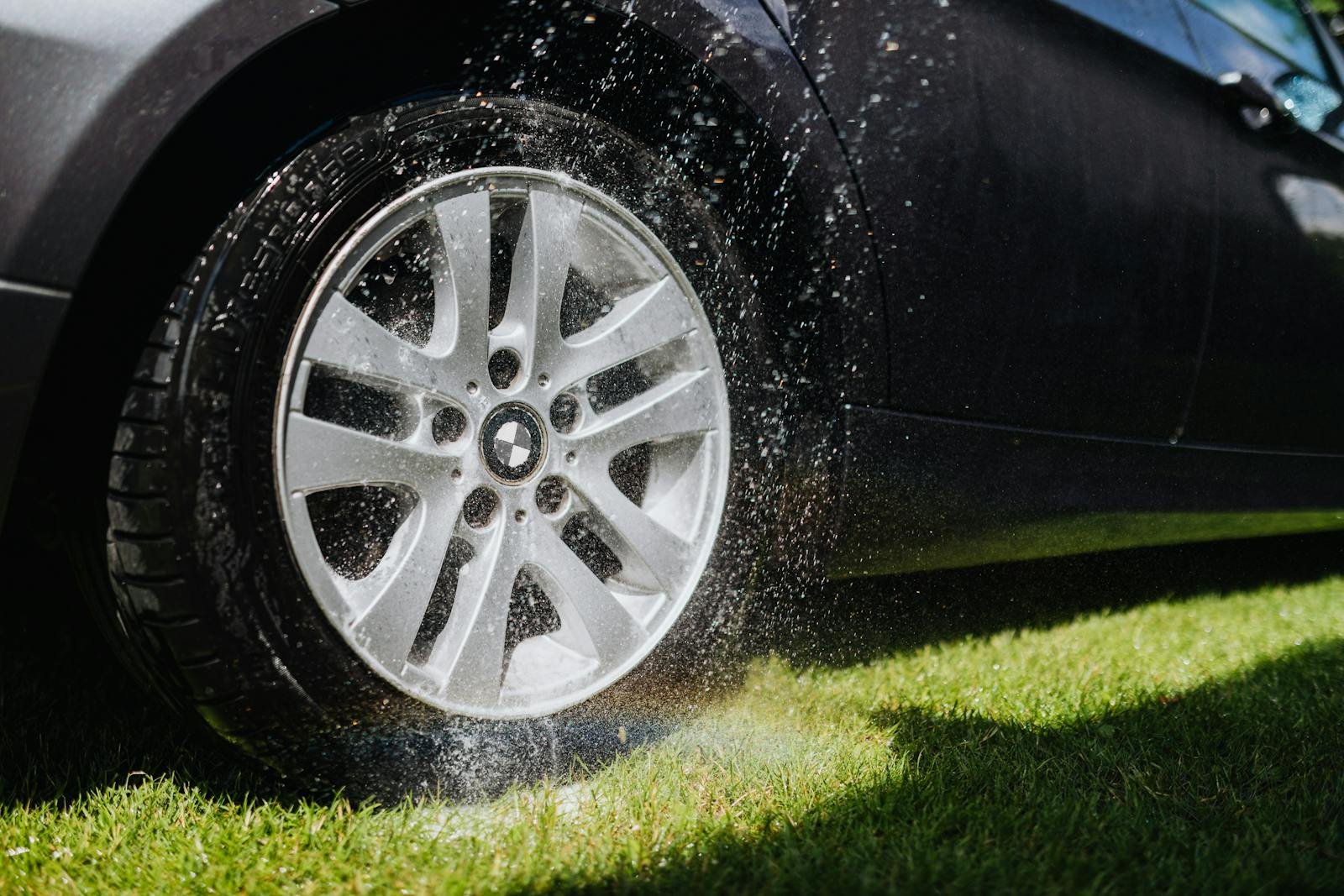 Dynamic image of a car wheel being hosed down during a wash on green grass.