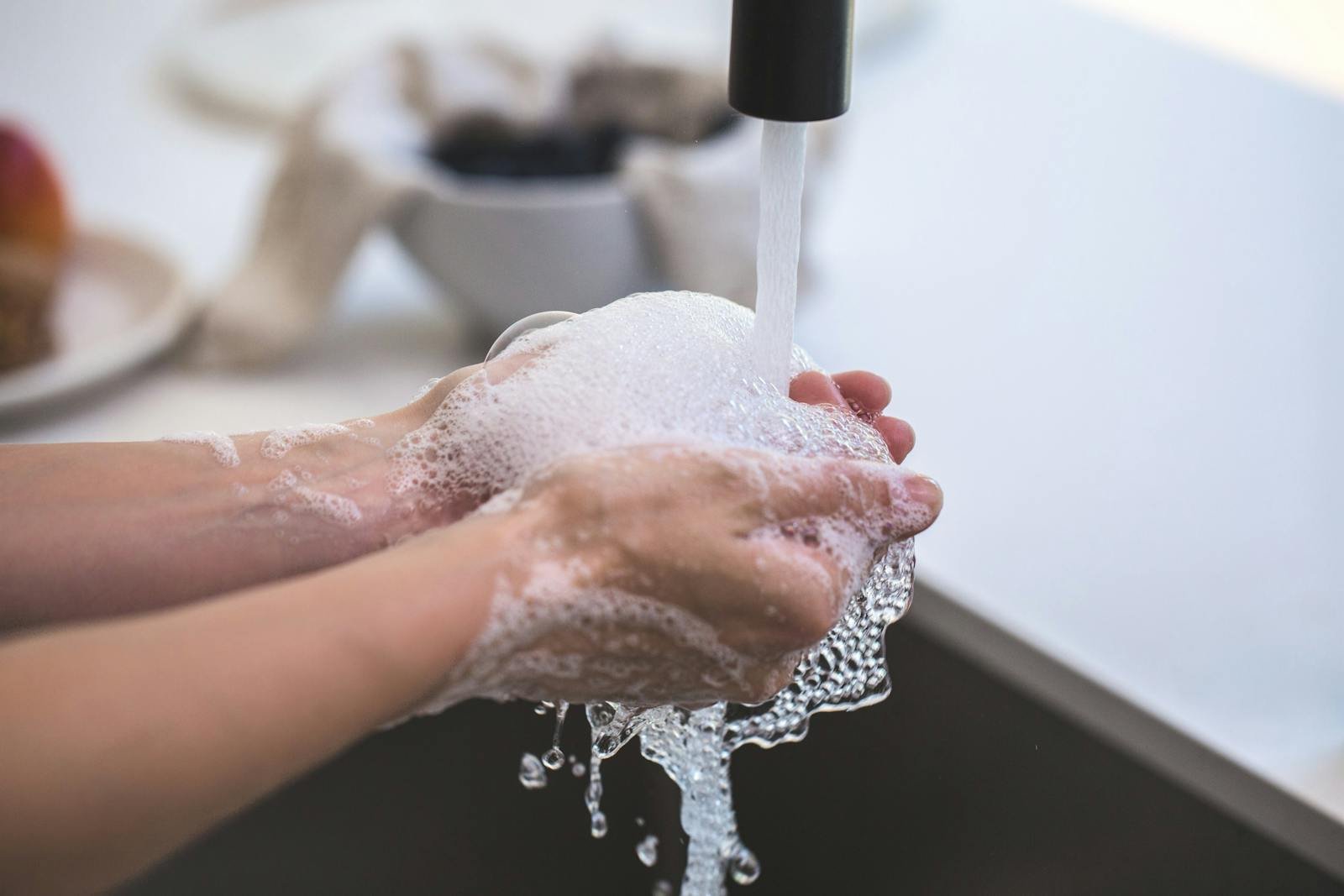 Close-up of hands being washed with foamy soap under a faucet, highlighting hygiene and cleanliness.