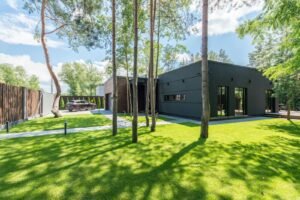 Contemporary house surrounded by lush green yard and trees, on a sunny day.