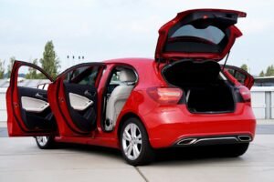 Red hatchback with open doors parked on pavement in the UK, showcasing the car interior and trunk space.