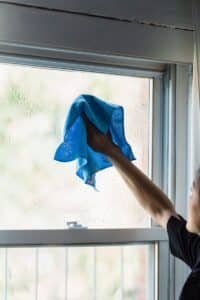 Person cleaning window with a blue cloth inside a home. Bright and minimalistic.