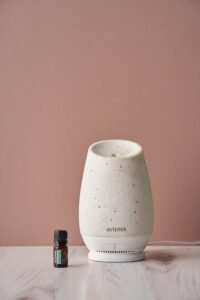 A stylish diffuser and essential oil bottle on a wooden table set against a pastel backdrop.