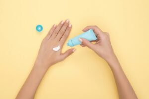 Close-up of a woman's hands applying cream on a pastel yellow background. Ideal for beauty and skincare themes.