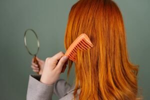 Close-up of a woman with red hair combing while holding a mirror.