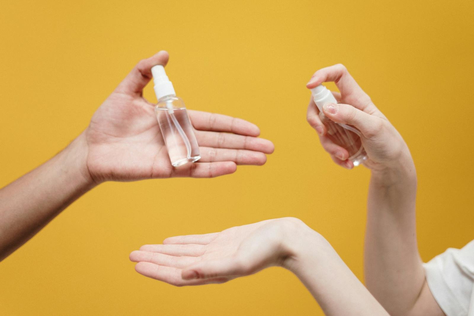 Hands using hand sanitizer against a yellow background, highlighting hygiene.