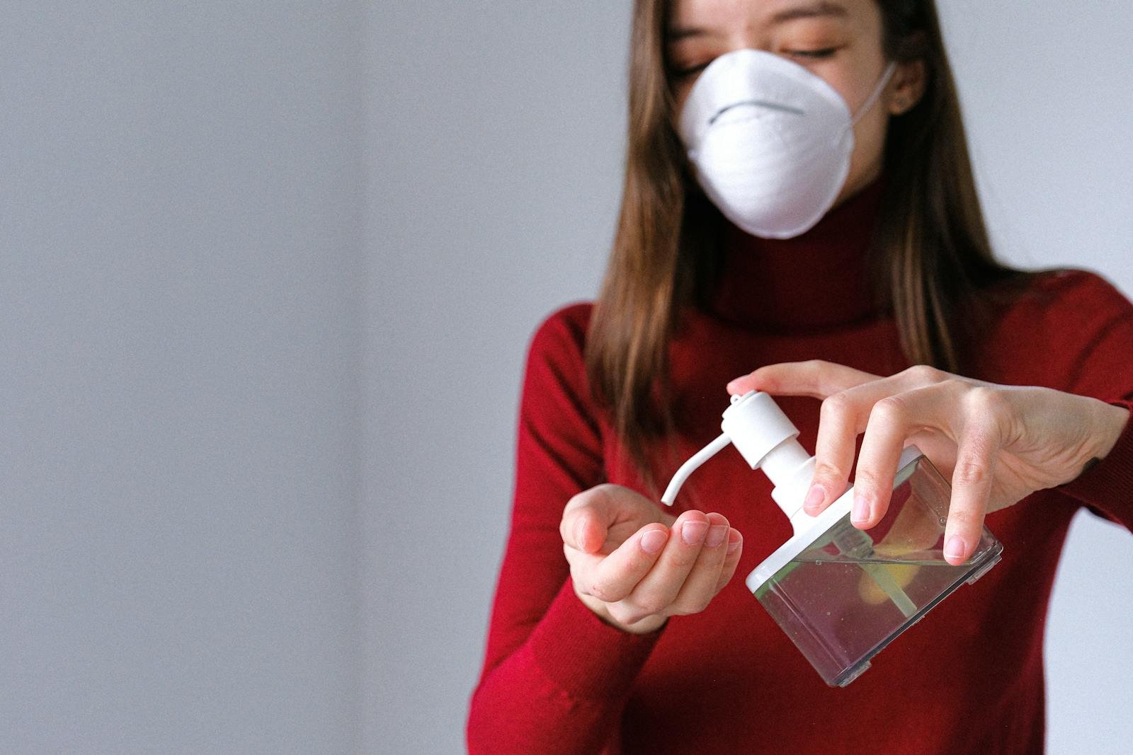 A woman in a mask applies hand sanitizer for hygiene indoors during pandemic.