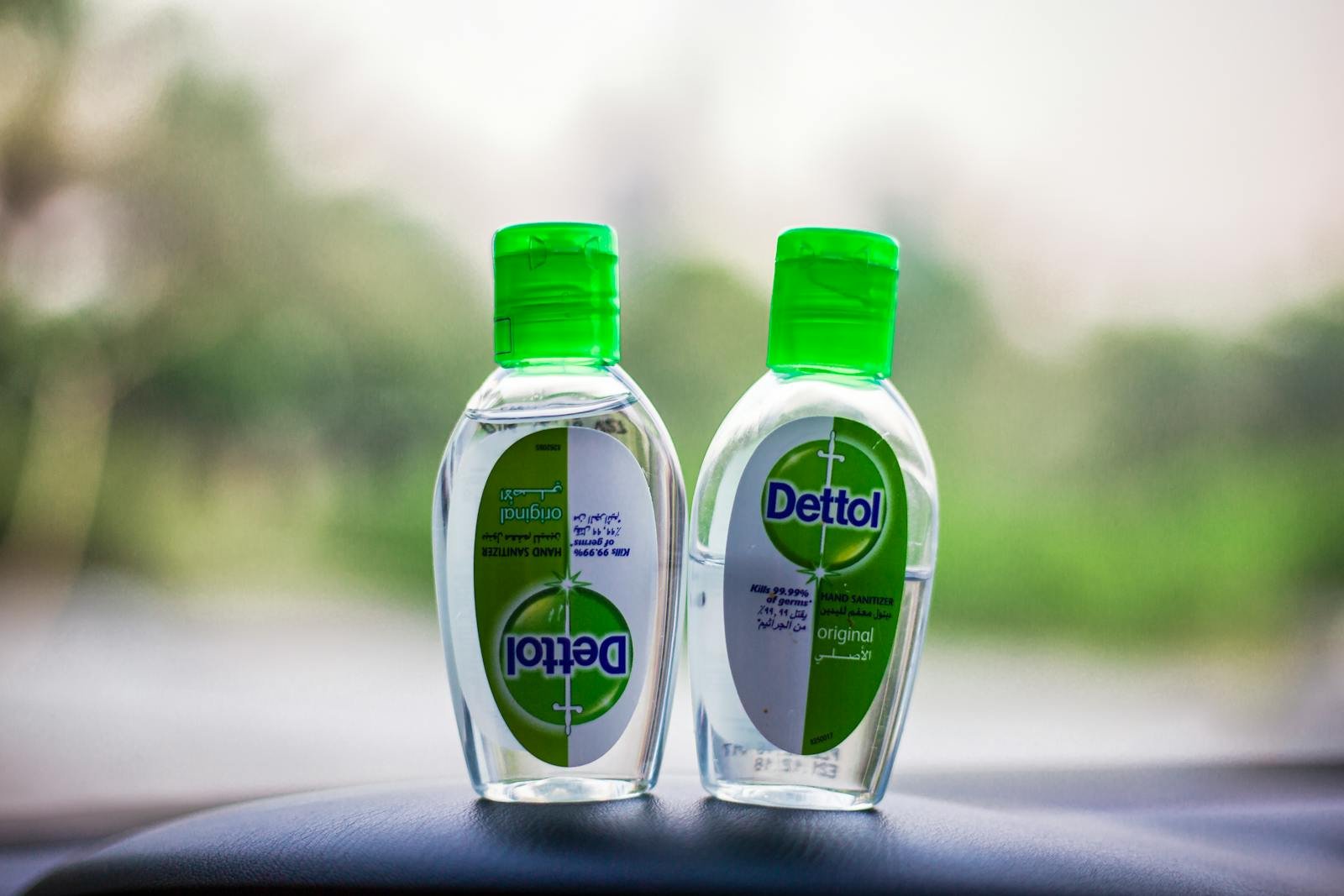 Clear Dettol hand sanitizer bottles, green caps, health focus outdoors with blurred background.