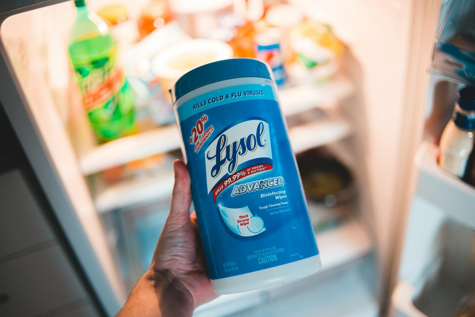 High angle of crop faceless person holding container of antibacterial wipes near opened fridge during housework