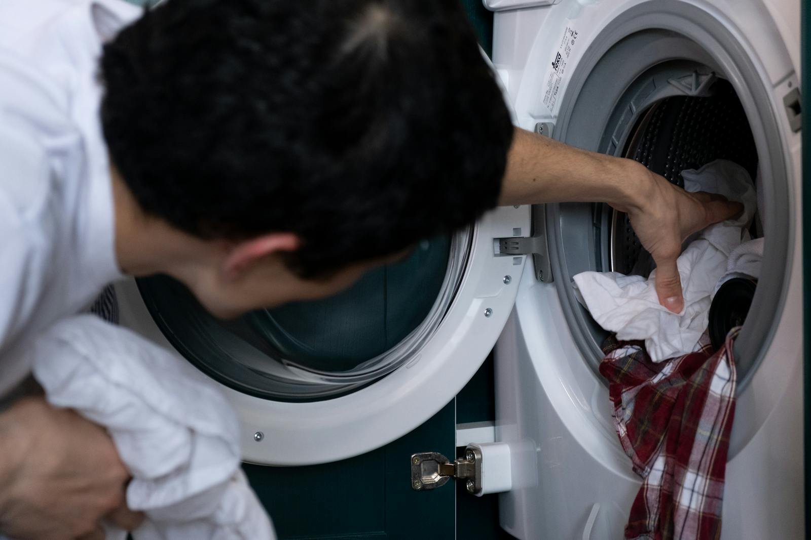 Close-up of a man placing clothes into a washing machine during household chores.