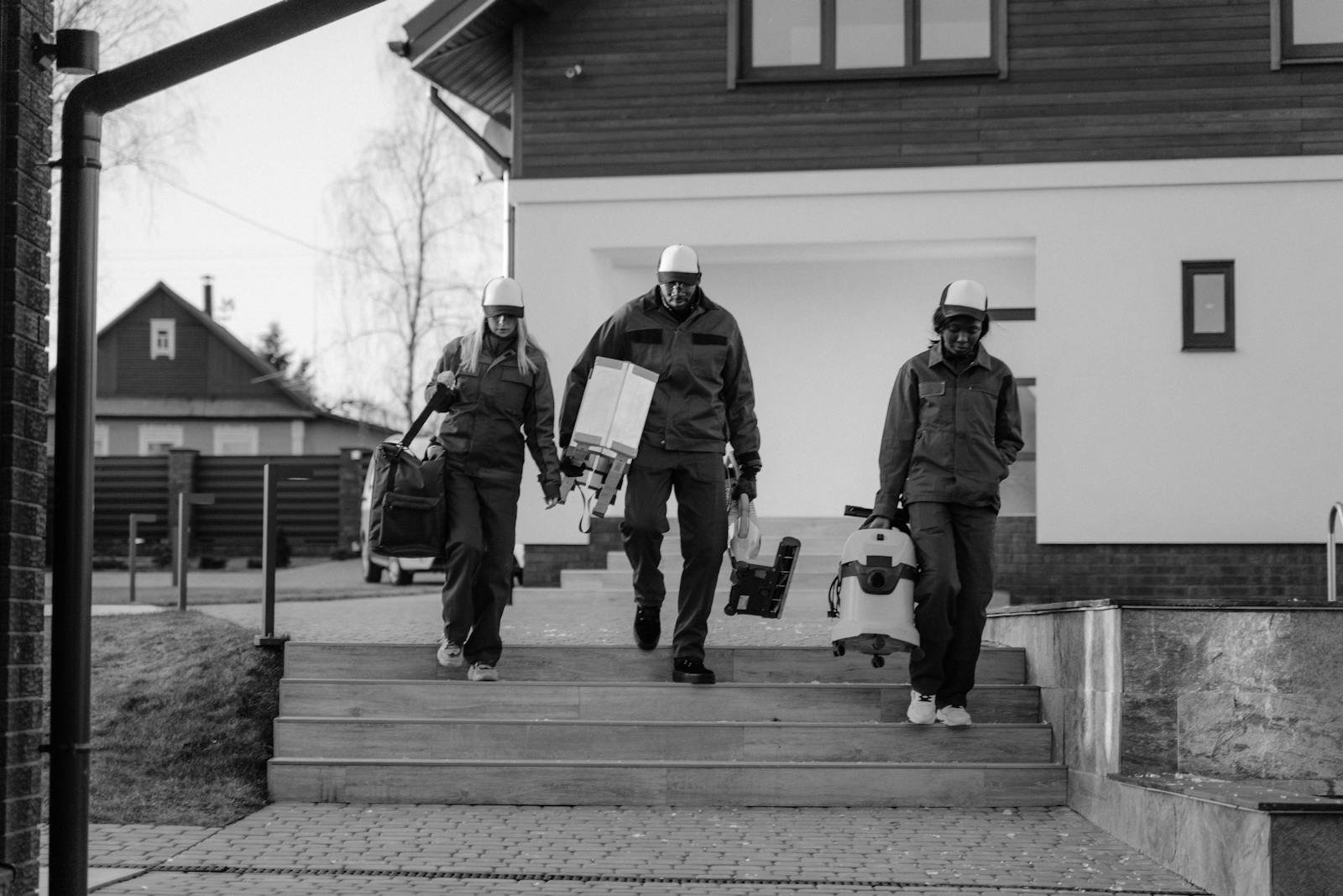 Three construction workers in safety uniforms and helmets walking outside a building.