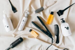 Flat lay image of various hair care products and tools on a textured fabric surface.