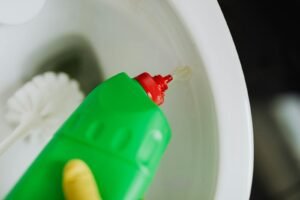 A person wearing a glove pours cleaning liquid into a toilet for sanitation.