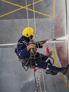 A worker in safety gear high up cleaning a building with a pressure washer in Dubai.