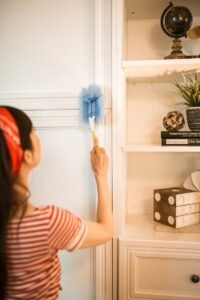 A woman dusting shelves at home, showcasing a tidy and clean living space.