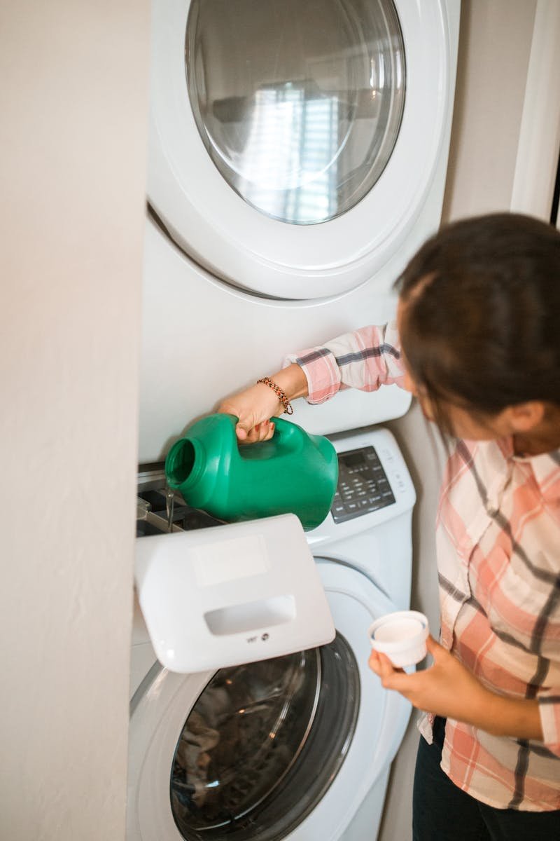 A woman in checkered sleeves adding detergent to a white washing machine.