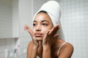 Young woman practicing skincare routine with a towel wrap indoors.